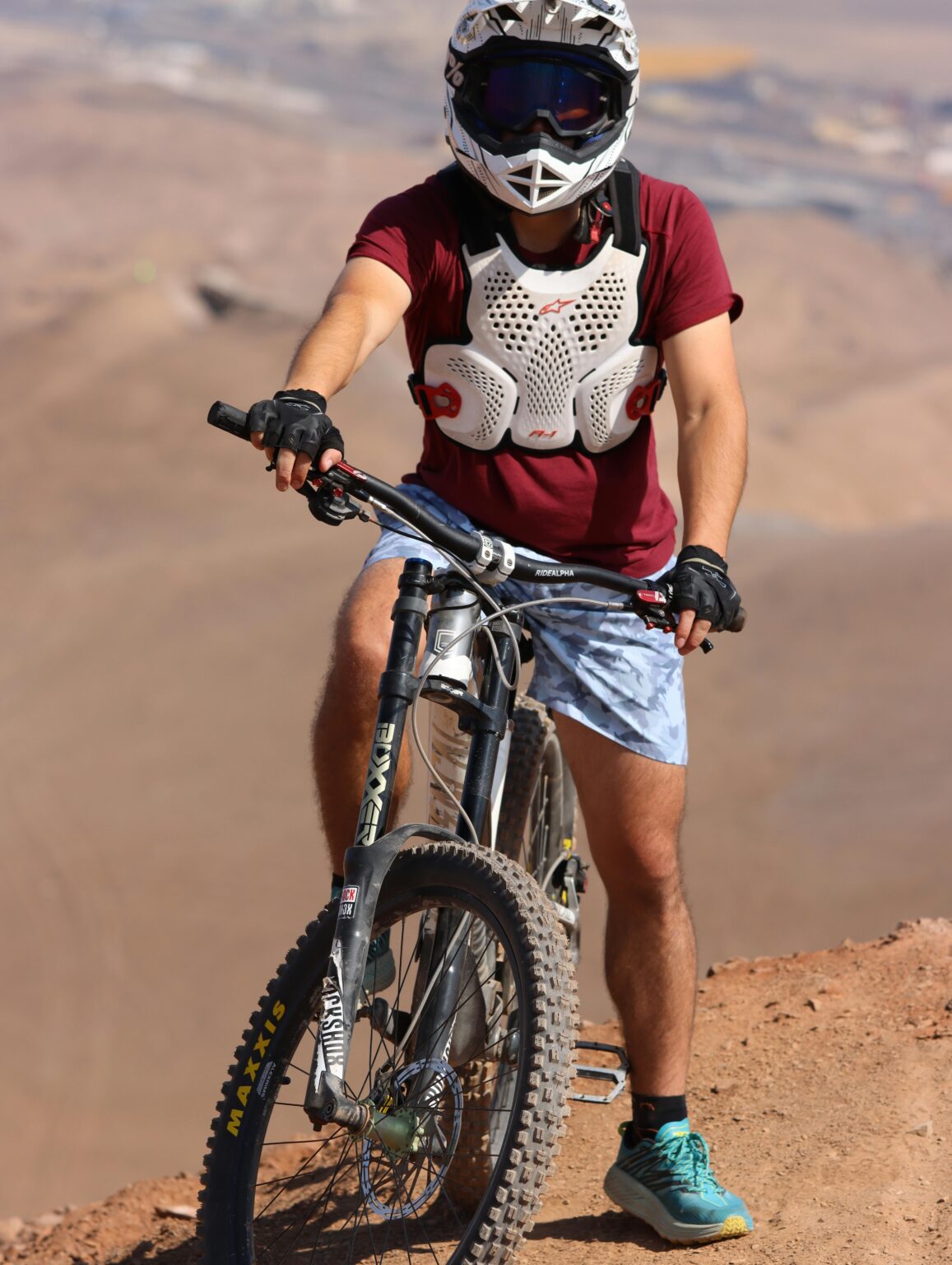 Mountain biker wearing helmet and chest armor on arid desert trail during sunny day.