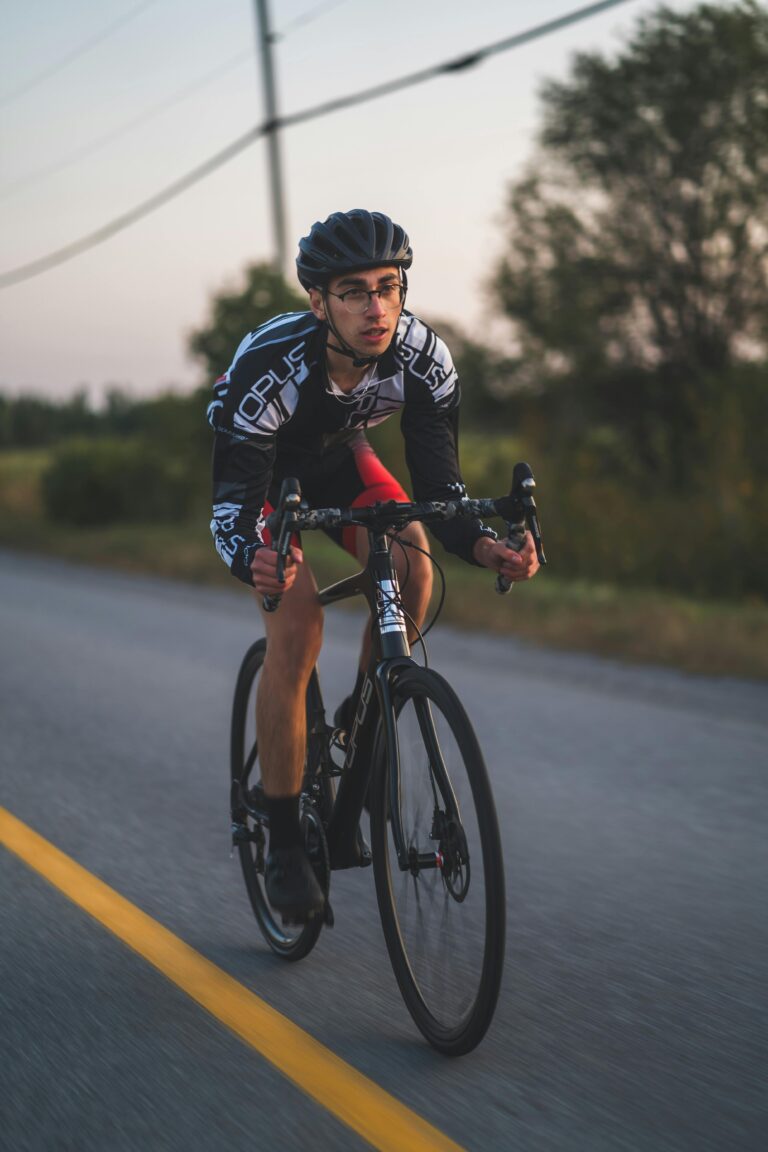 A cyclist wearing gear rides swiftly on an open road during dusk, showcasing speed and determination.